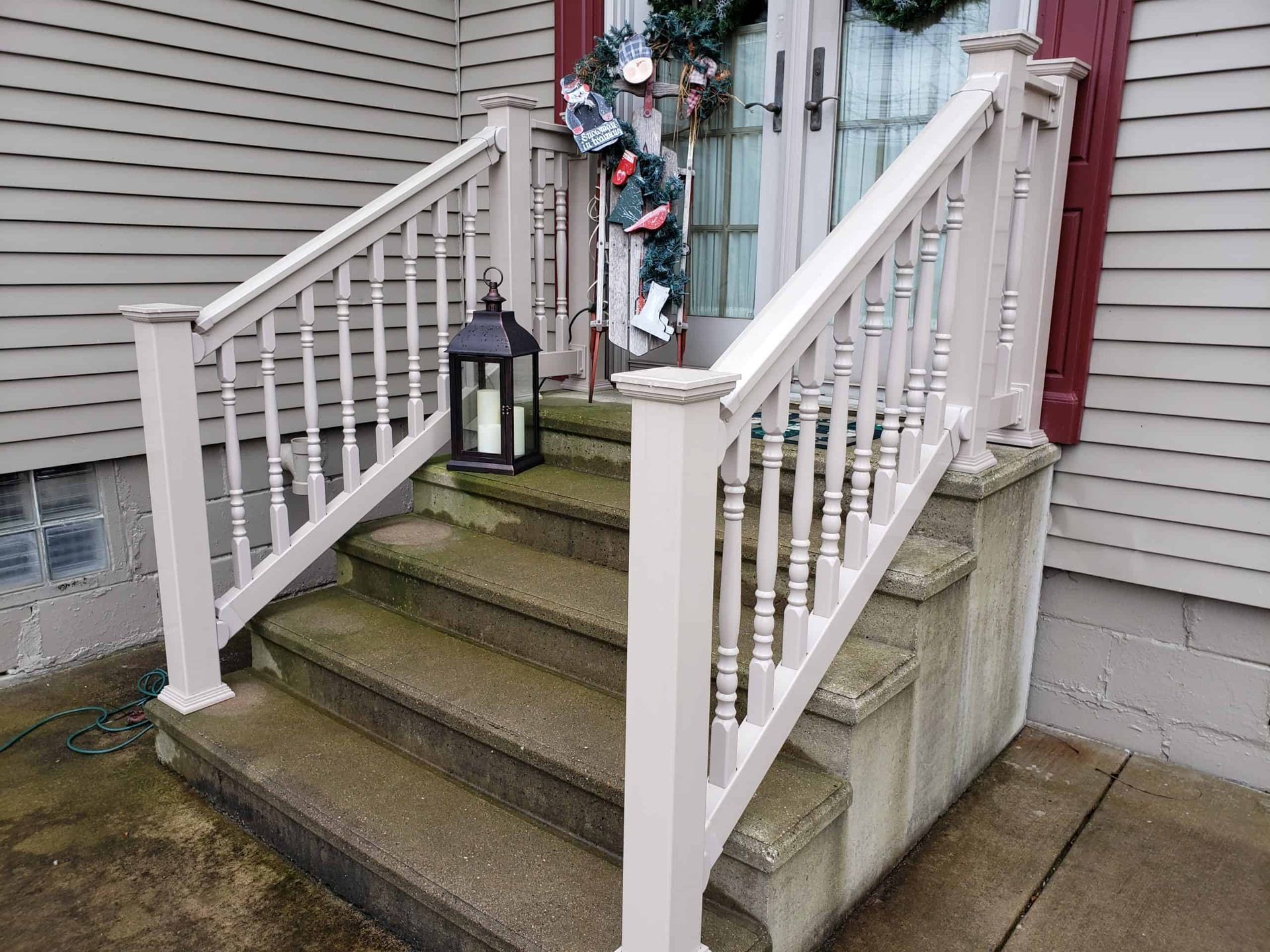 Front steps with white railings, a black lantern, and festive holiday garland by a house entrance
