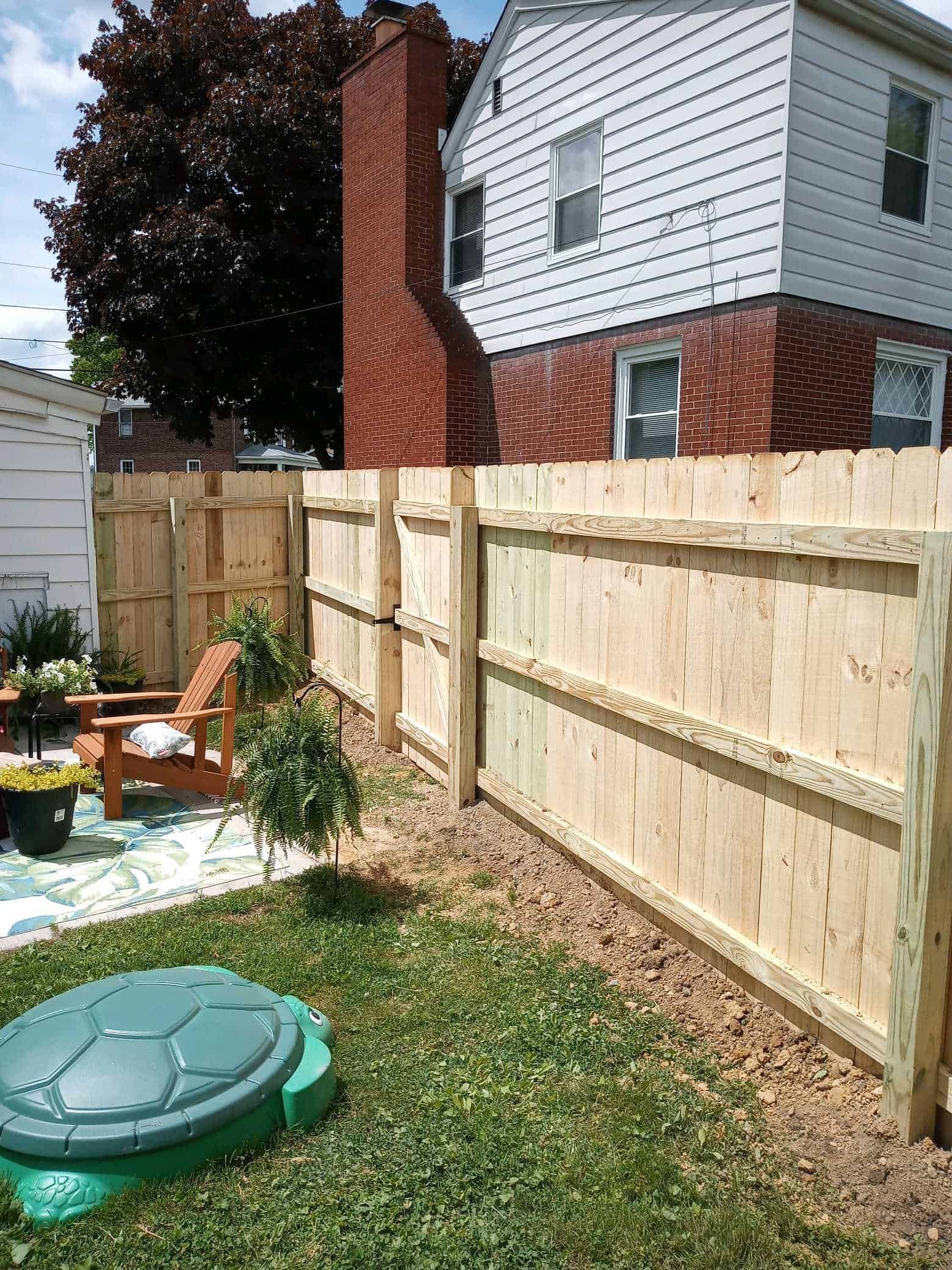 Backyard with wooden privacy fence, grass lawn, patio chairs, and a green turtle sandbox cover