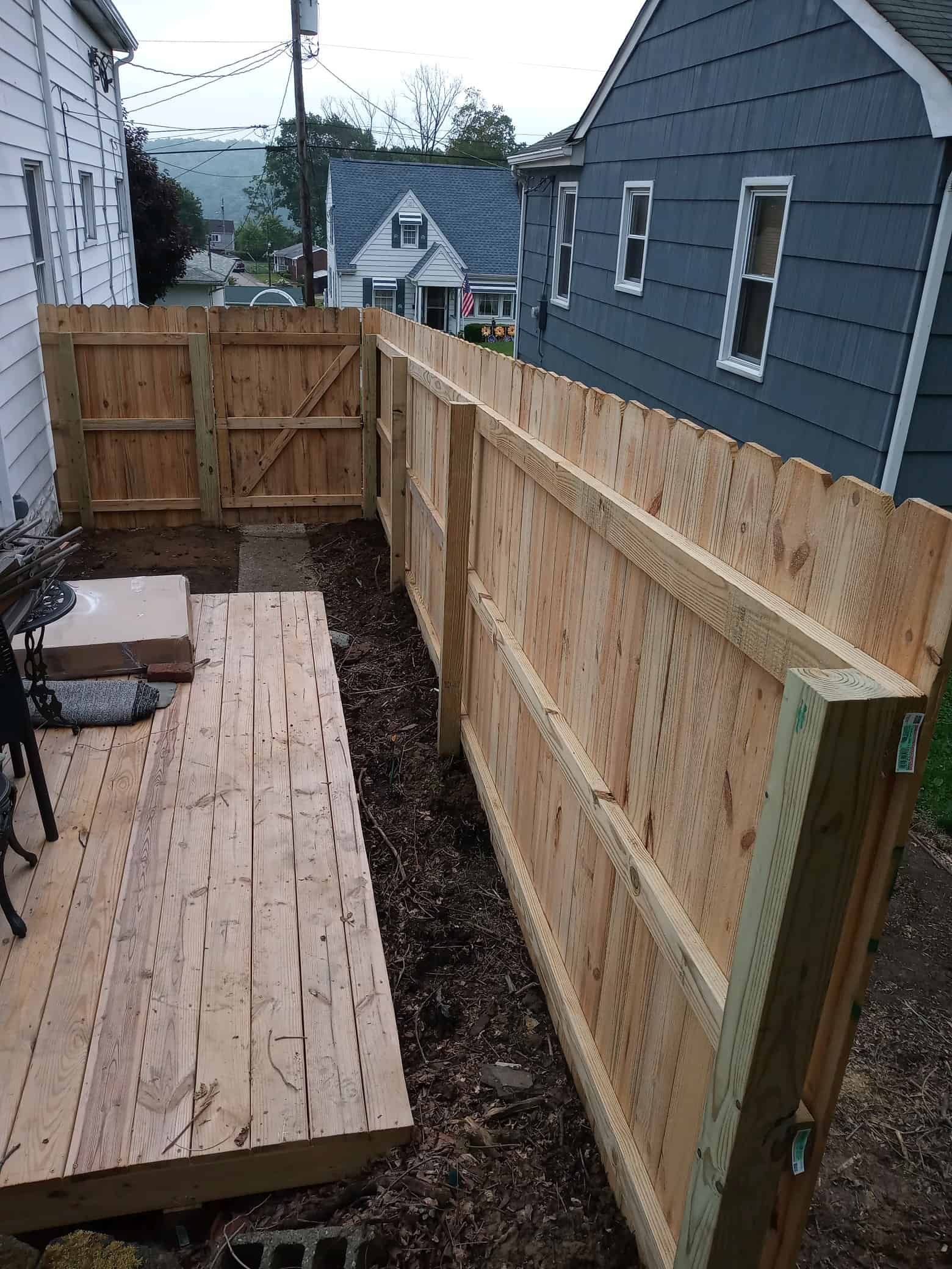 Narrow wooden side yard with a raised deck walkway, fence, and small gate between two houses