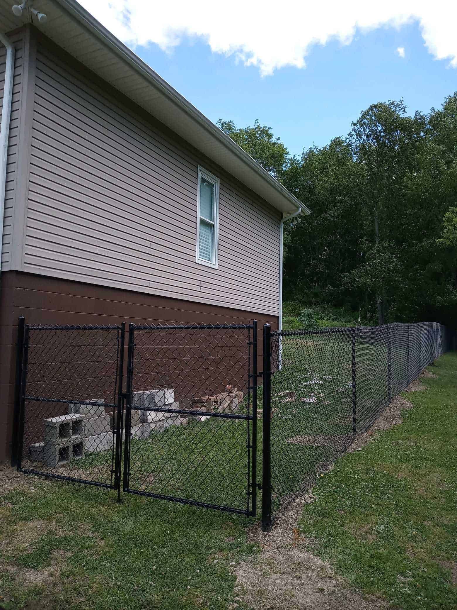 House side with white lattice siding, black chain-link fence, and grassy yard beside trees