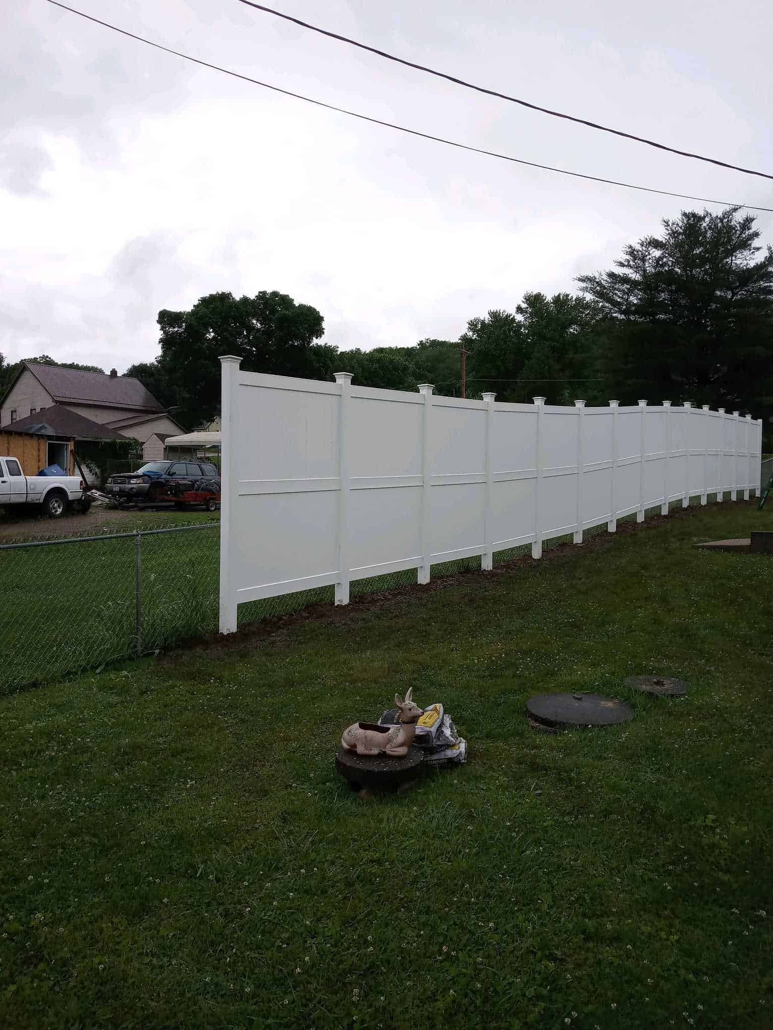 Long white fence panels stretching across a grassy yard beside a house under a cloudy sky