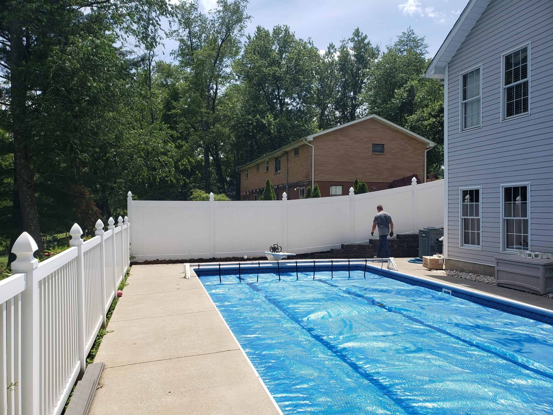 Backyard swimming pool covered with a blue tarp beside a white fence and house