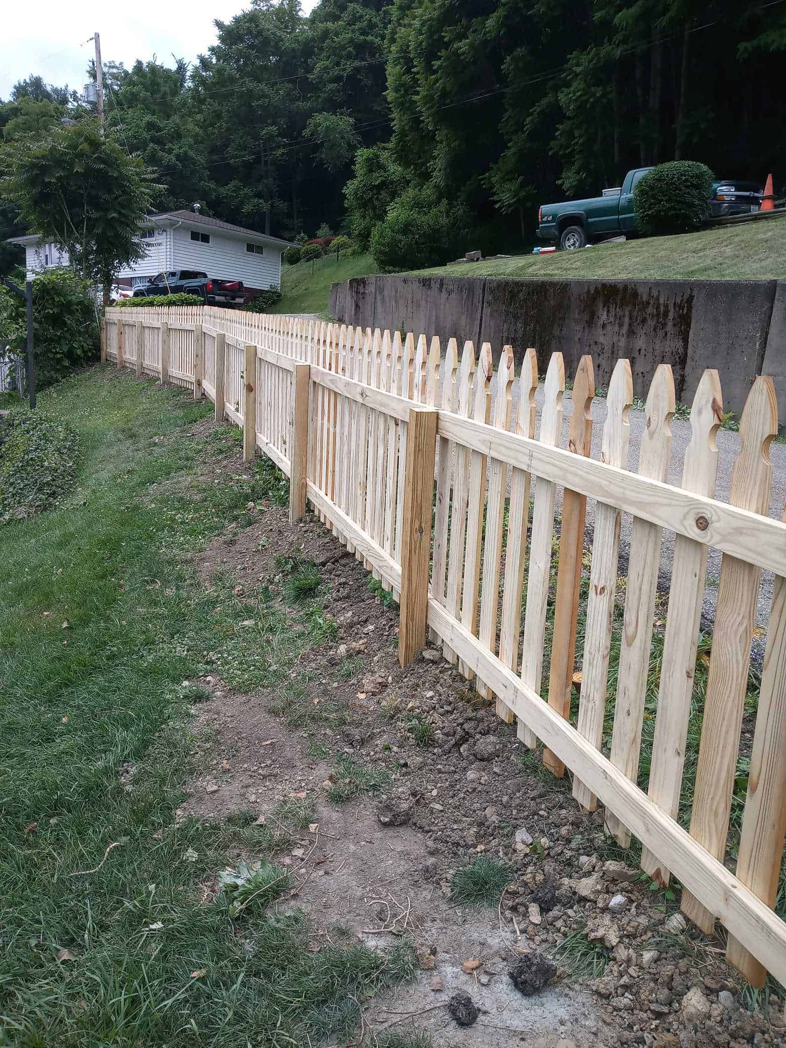 Fresh wooden fence running along a grassy path beside a concrete wall and trees