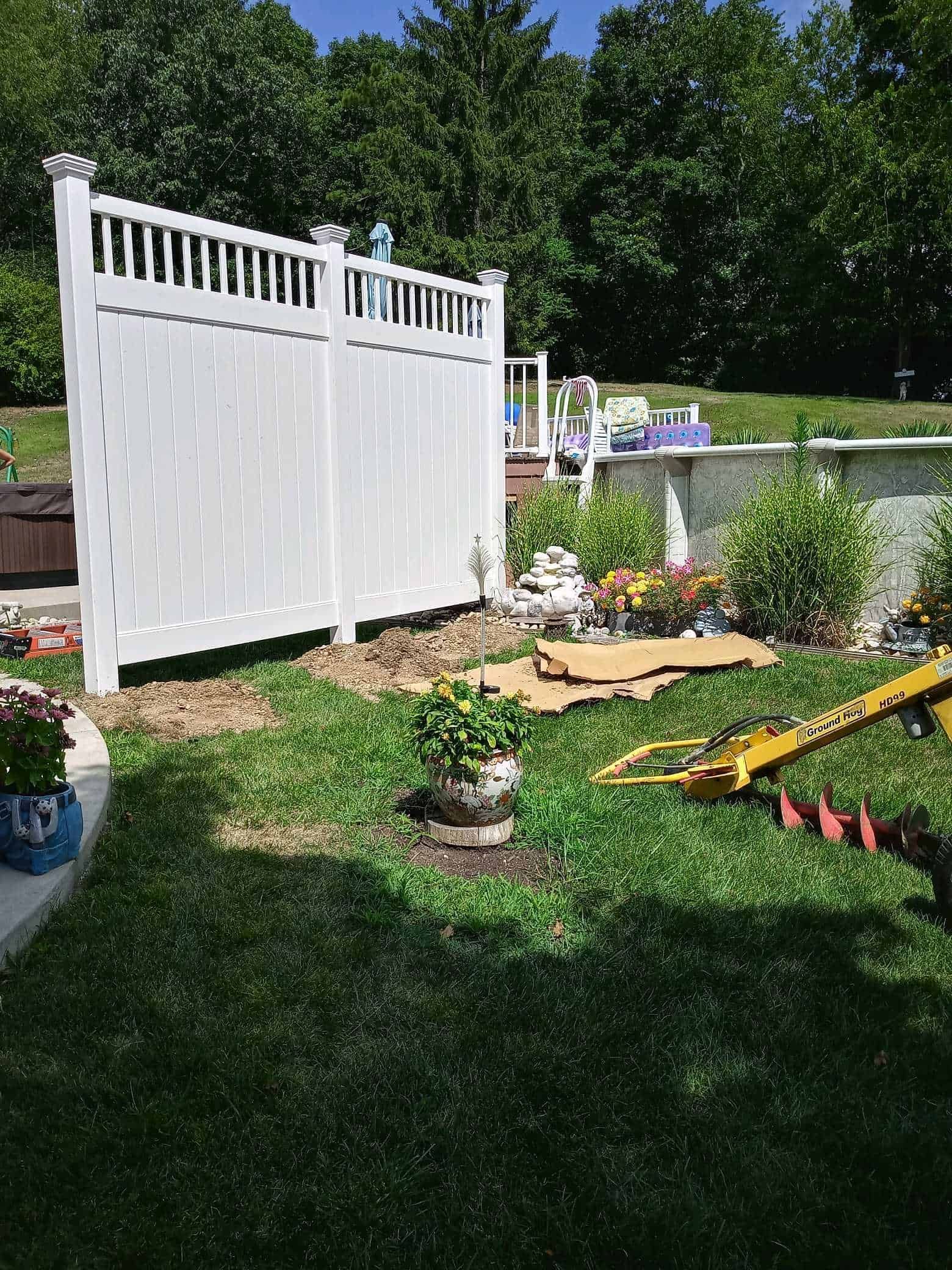 White garden fence beside a flower bed and lawn, with trees in the background.