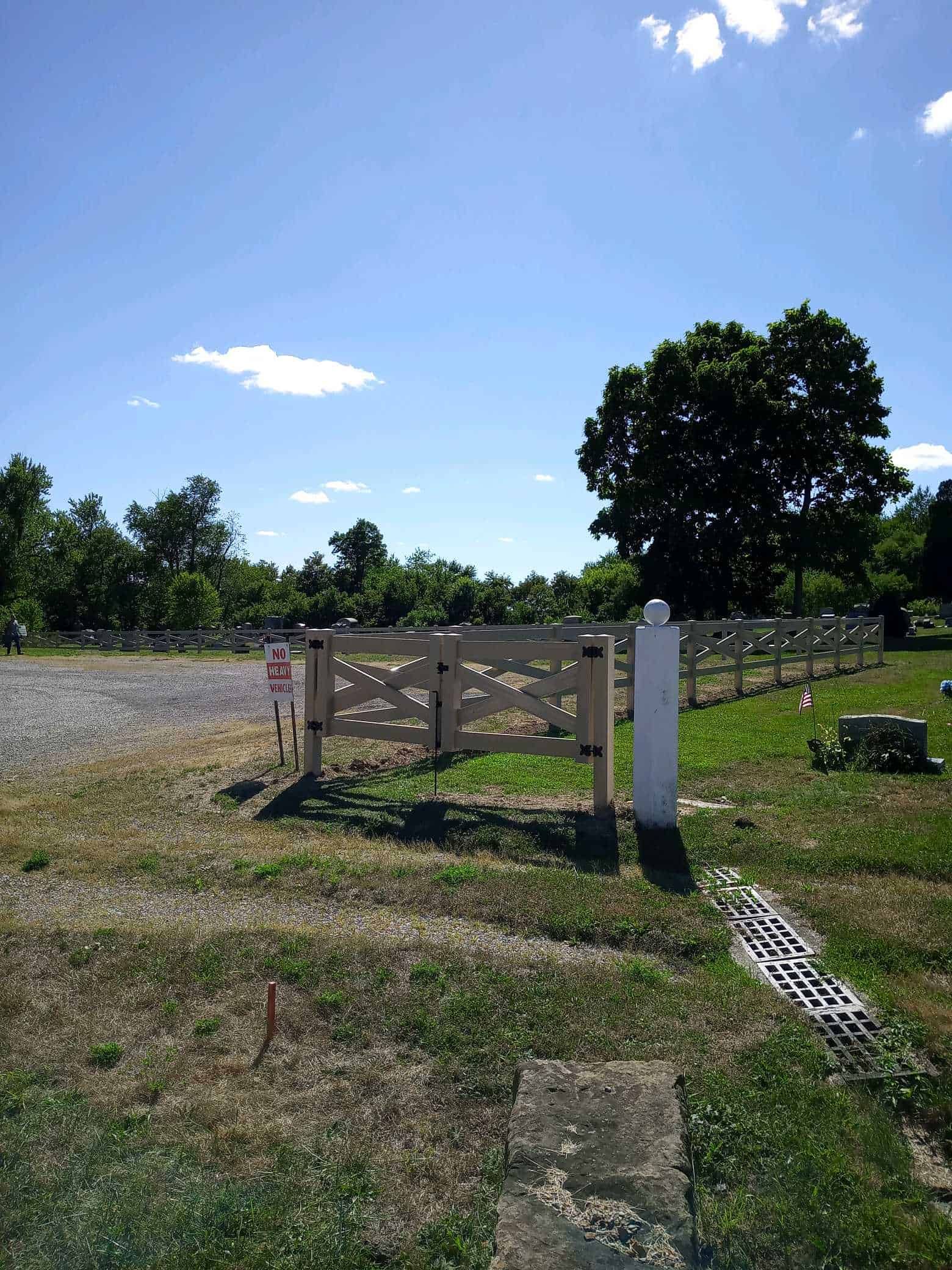 Wooden fence gate in a sunny grassy field under a blue sky with trees in the background