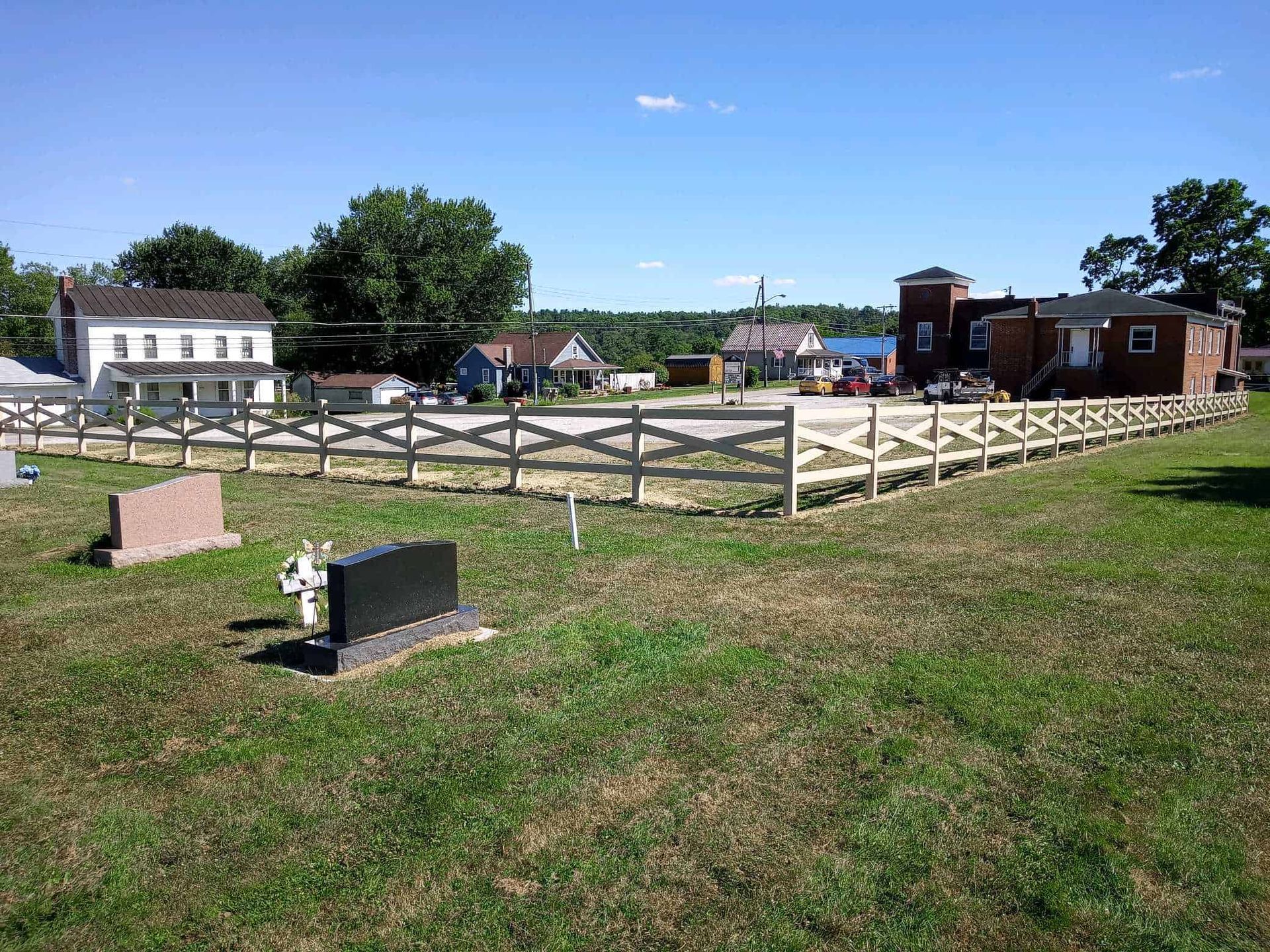 Outdoor memorial site with fenced stone foundation, small monument, and buildings under a clear blue sky