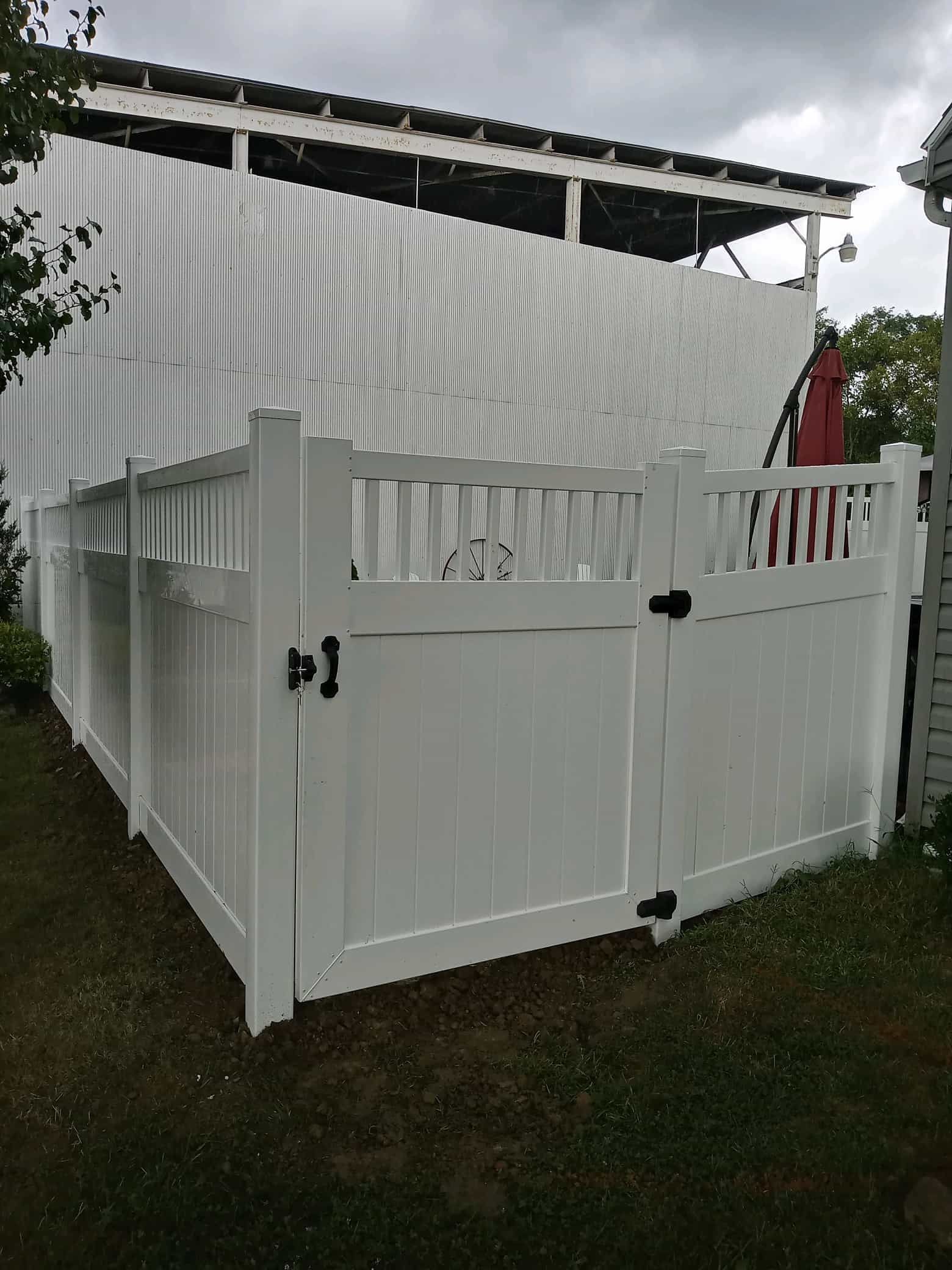 White fenced outdoor enclosure beside a corrugated shed under a cloudy sky