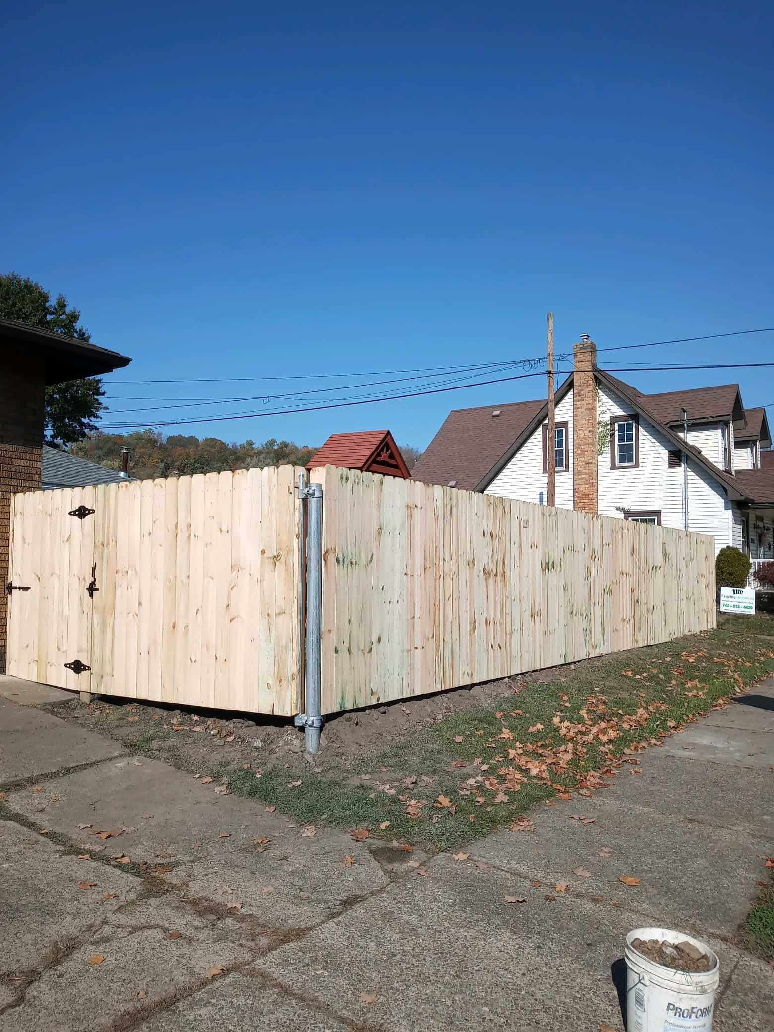 Wooden privacy fence around a corner lot beside a sidewalk and houses under a clear blue sky
