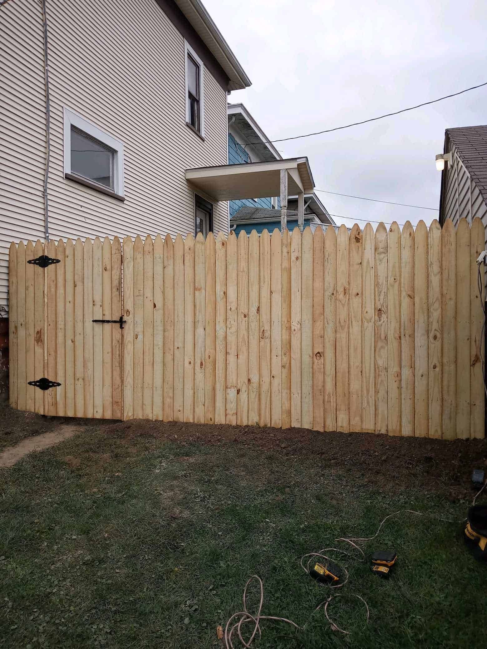 Wooden backyard fence with a gate beside a house and grass in the foreground