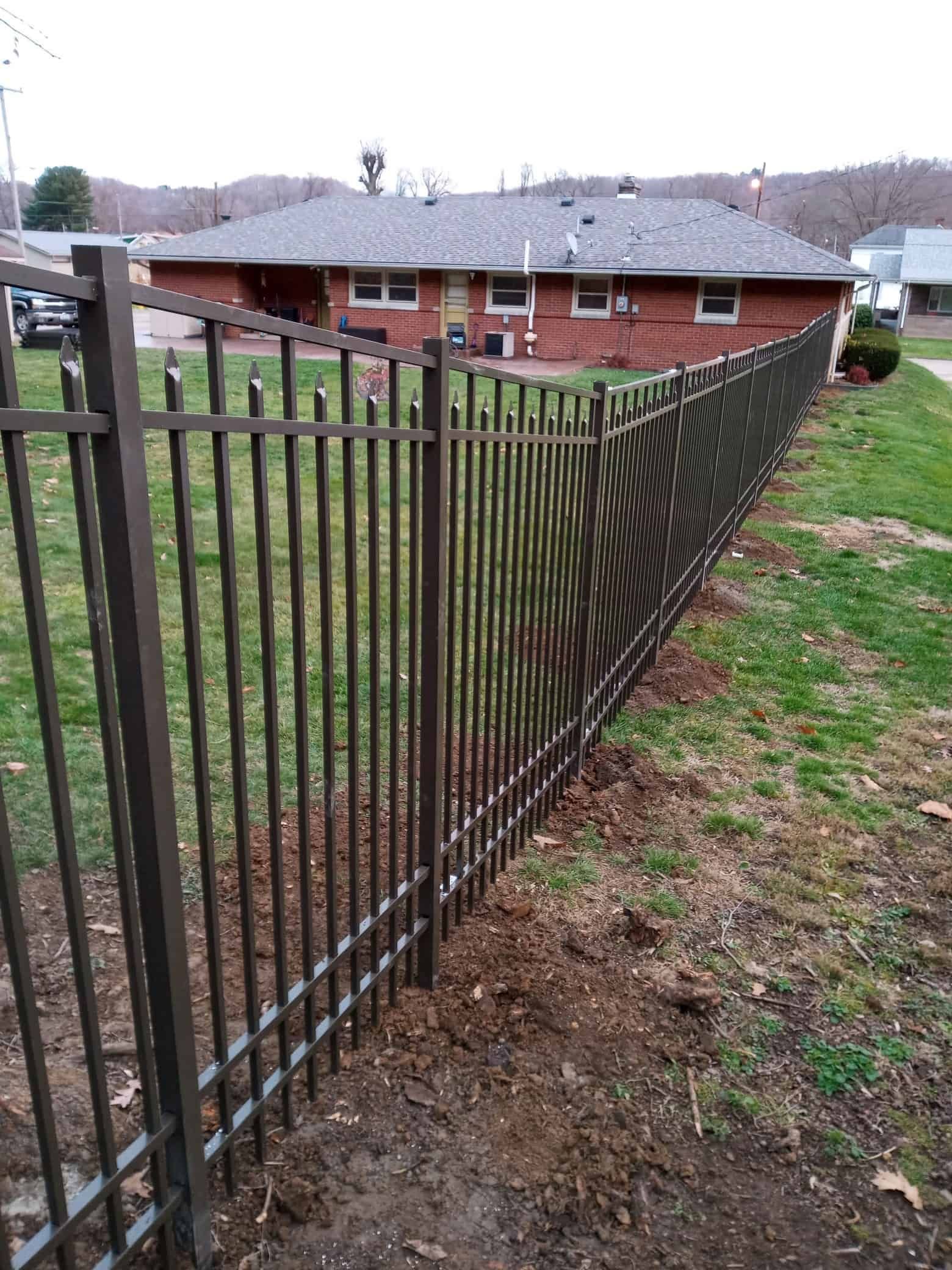 Black metal fence along a grassy yard beside a brick apartment building on a cloudy day