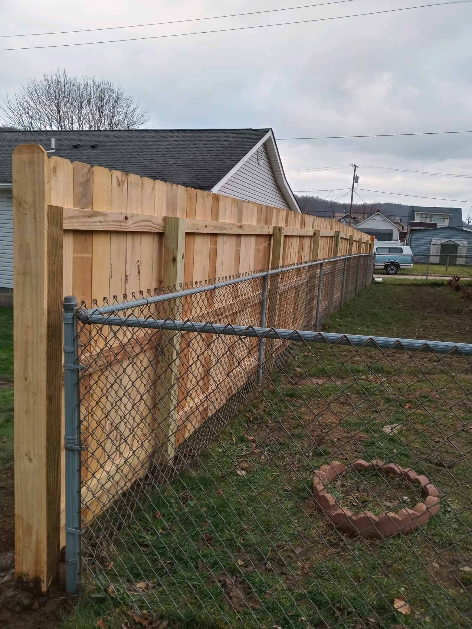 Wooden privacy fence beside a chain-link fence in a suburban yard under an overcast sky