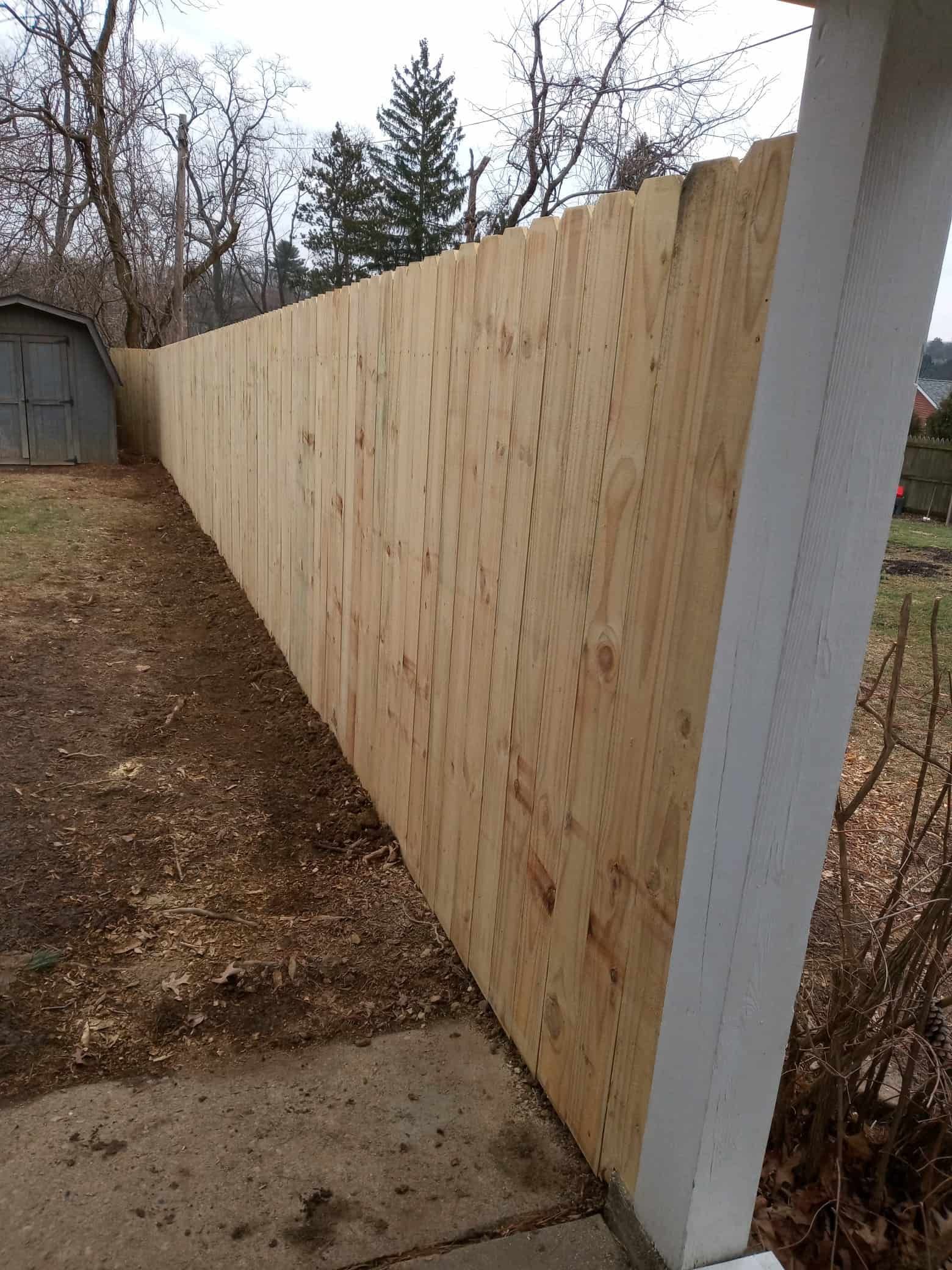 New wooden fence panel along a concrete path beside a white post and shed.