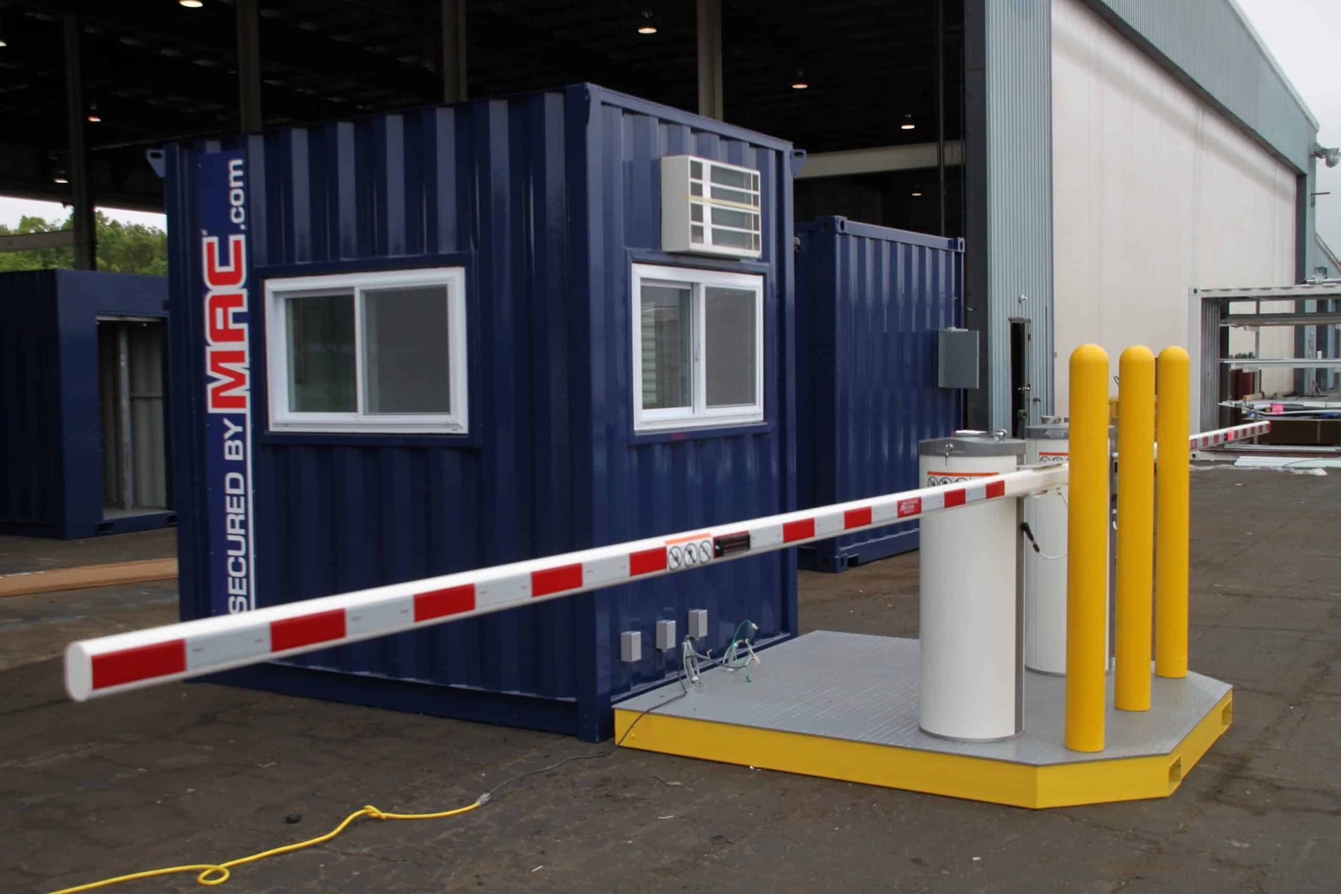 Red-and-white barrier arm blocking a small blue shipping-container booth with yellow bollards nearby