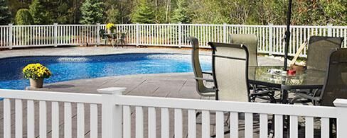 Backyard pool with white fence, patio chairs, and a table beside the water
