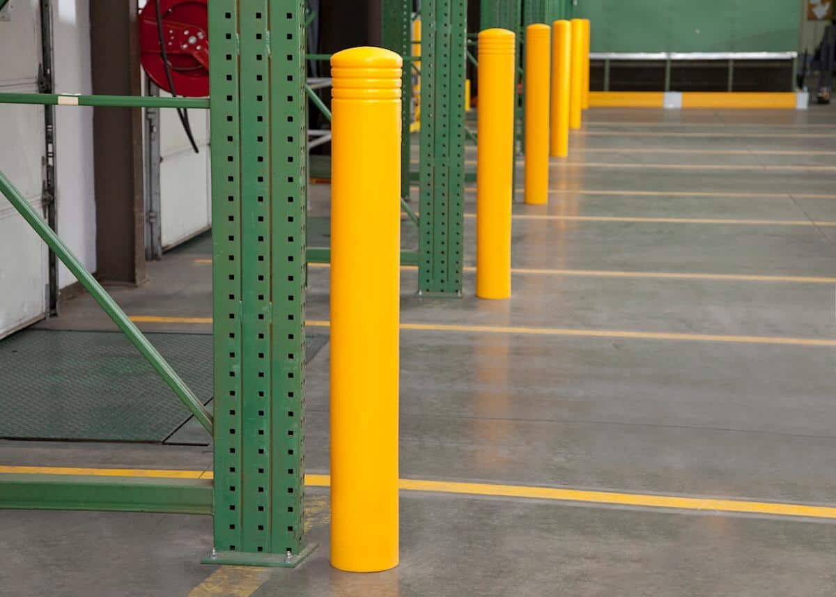 Yellow safety bollards beside green steel columns in an industrial warehouse aisle