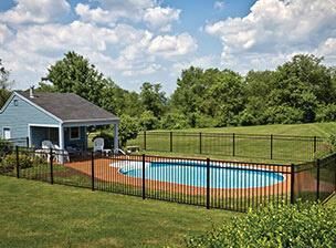 Backyard with an in-ground pool, black fence, and small blue pool house under a partly cloudy sky