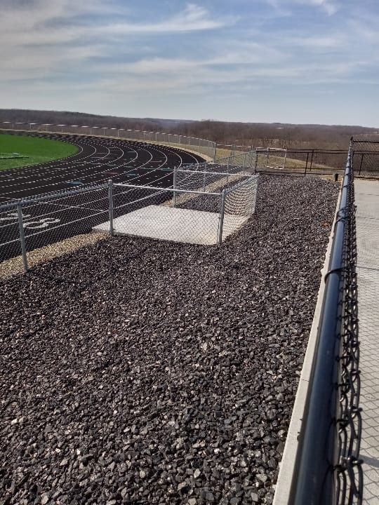 Chain-link fence beside an empty gravel track under a cloudy sky