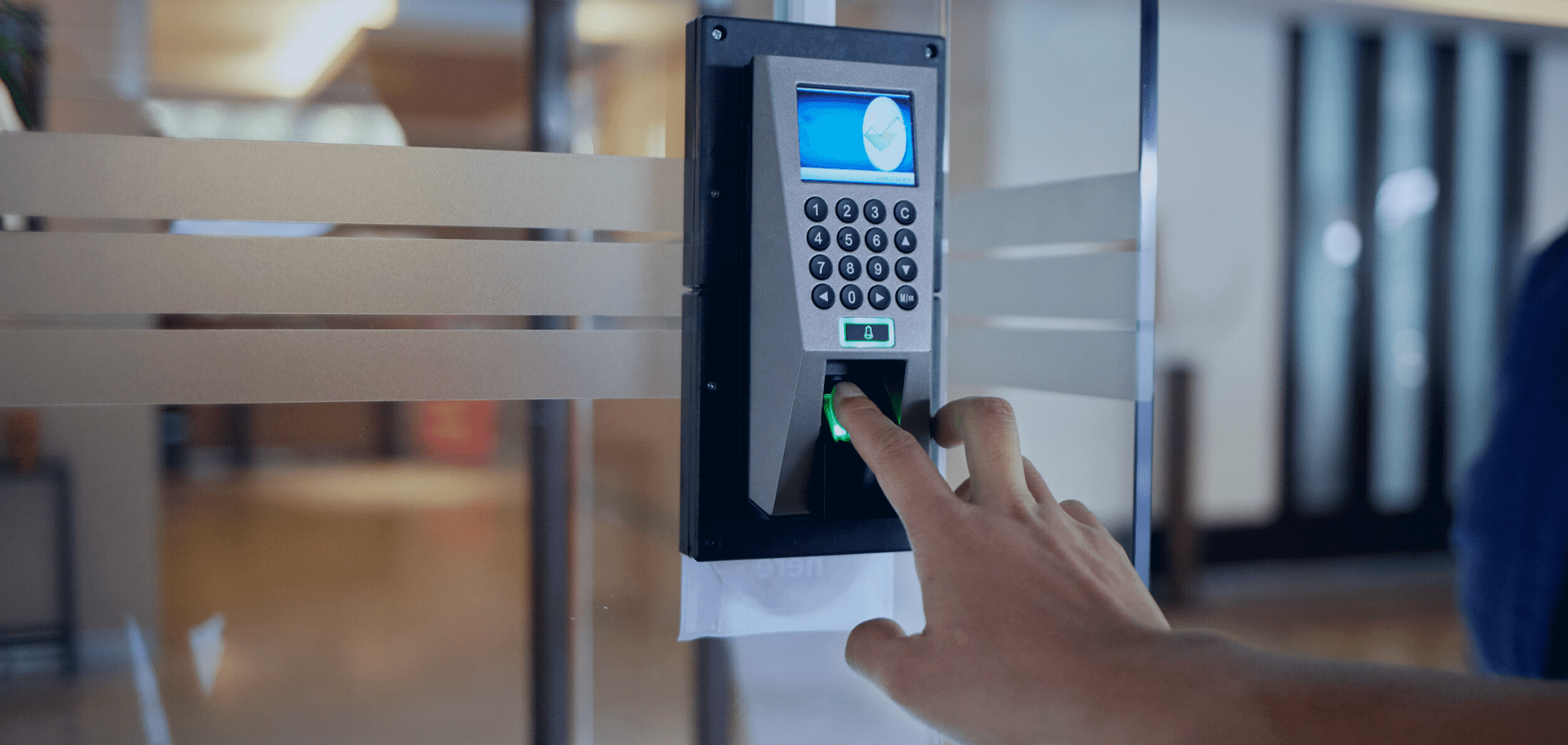 Hand pressing a fingerprint on a wall-mounted access control keypad with blue screen