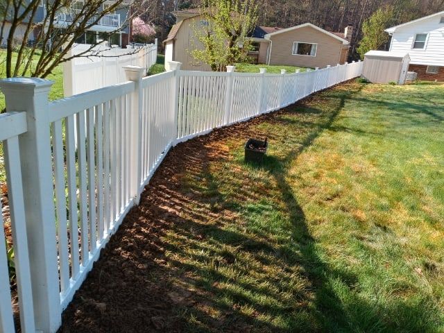White picket fence along a sunny suburban backyard with green lawn and neighboring houses