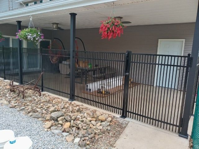 Covered patio with black metal fence, hanging flower baskets, and a hot tub beside rocks and sliding doors