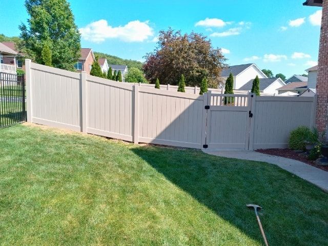 Backyard with beige vinyl fence, green lawn, and suburban houses under a blue sky