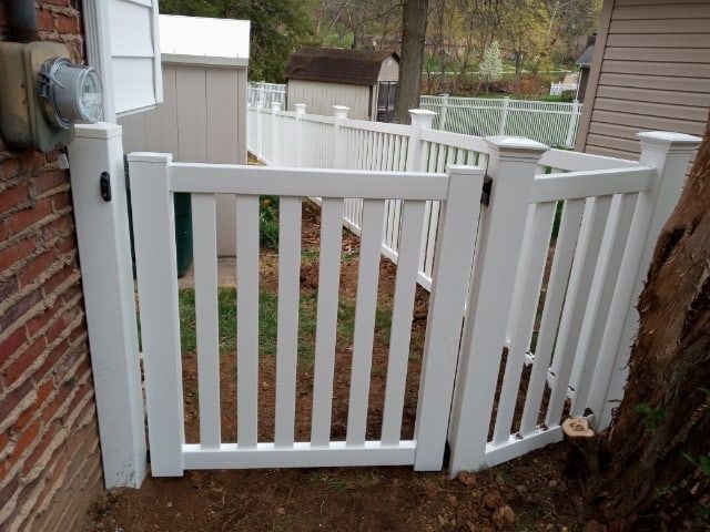 White garden gate between brick wall and tree in a fenced backyard