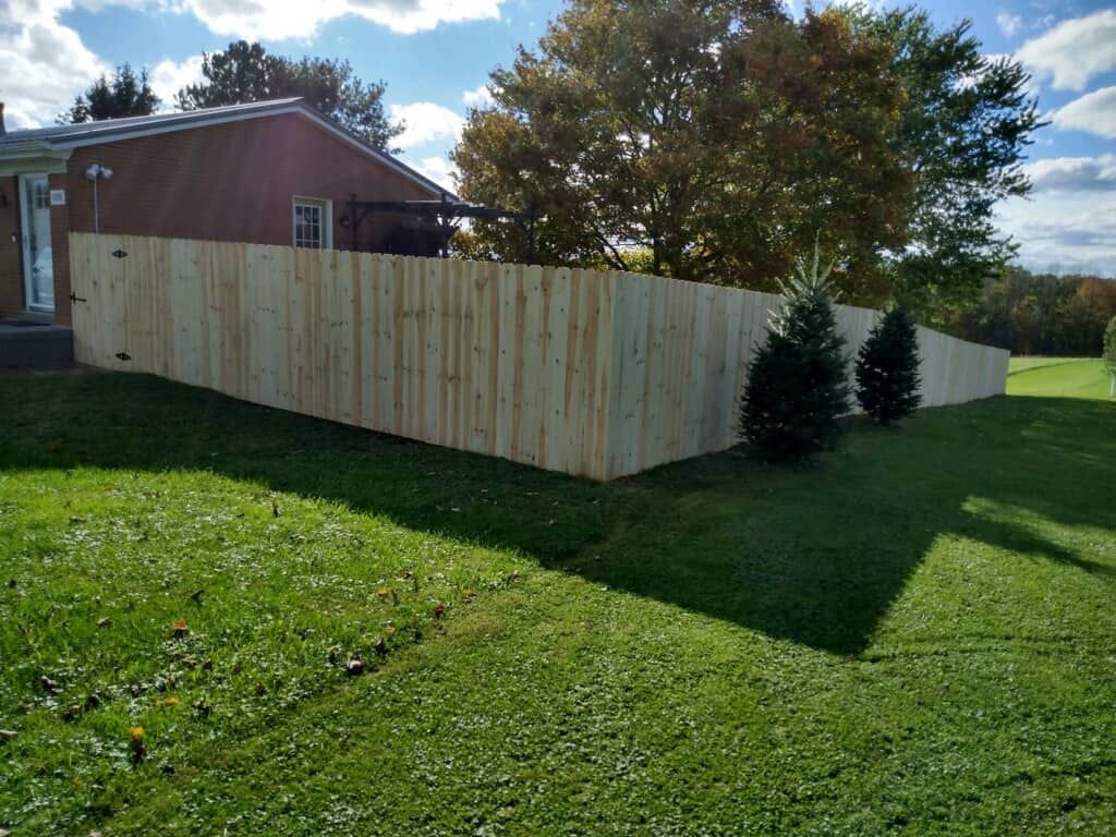Wooden privacy fence around a backyard beside a red house under a partly cloudy sky