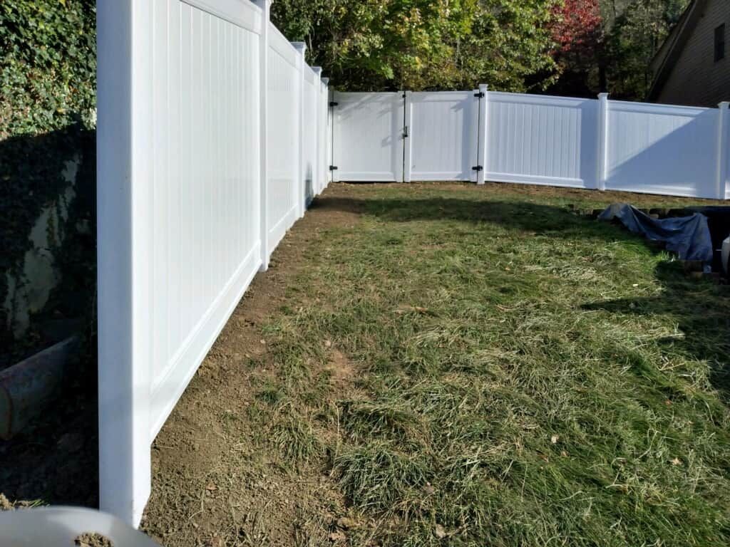 White vinyl fence beside a grassy yard with trees and a curved fence in the background