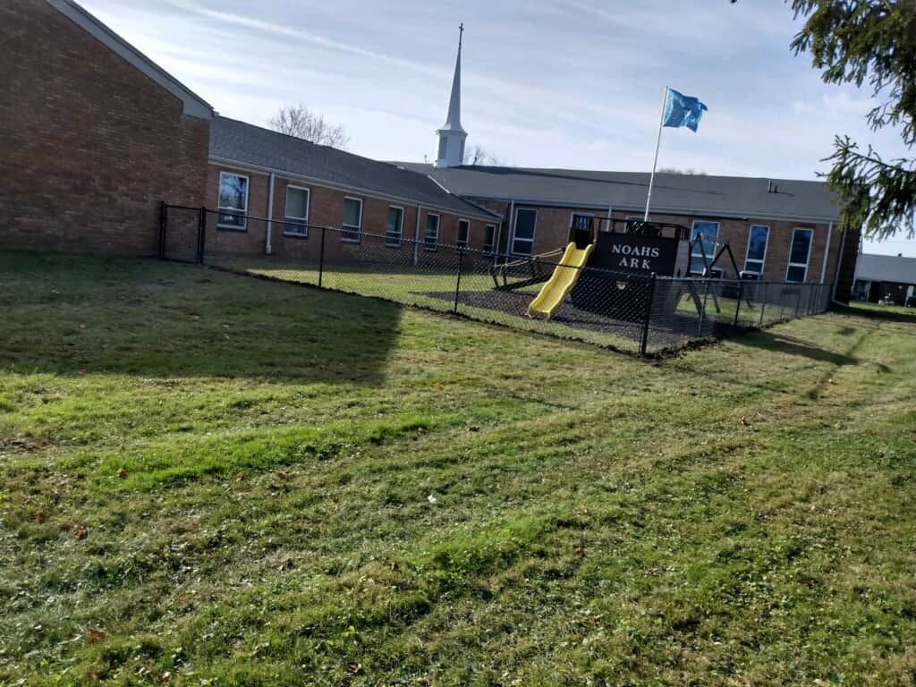Brick school building with grassy lawn, playground slide, and flagpole under a bright sky