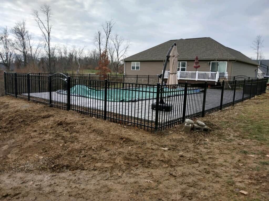 Backyard swimming pool surrounded by black fence, with patio and umbrella beside a house
