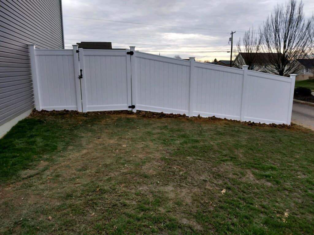 White vinyl fence enclosing a grassy yard beside a house under an overcast sky