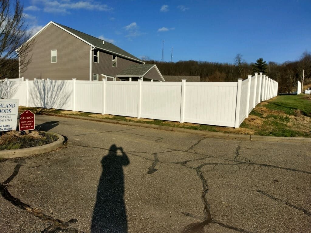 Suburban house with a tall white fence and cracked driveway under a blue sky