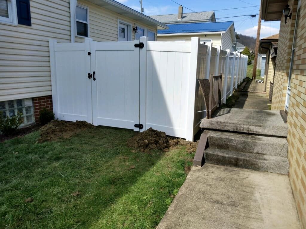 White vinyl fence beside a narrow concrete walkway between houses, with a small grass yard on the left
