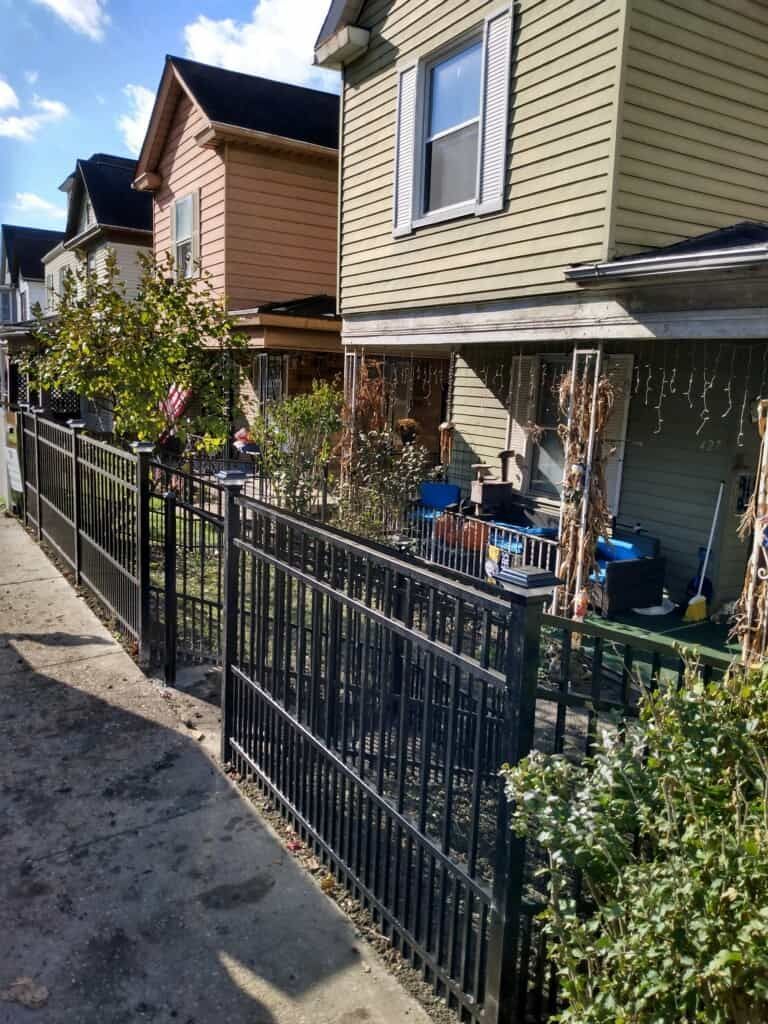 Narrow residential walkway beside row houses with black metal fencing and small front porches