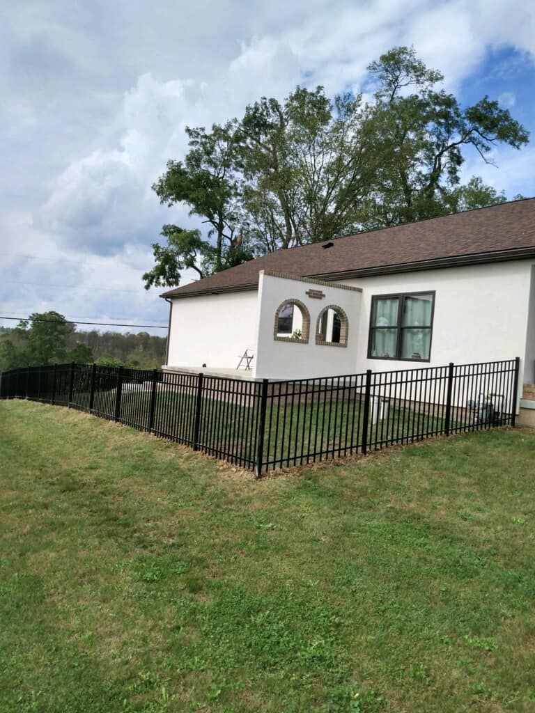 White house with red roof, arched windows, and black fence on a grassy lawn under cloudy sky