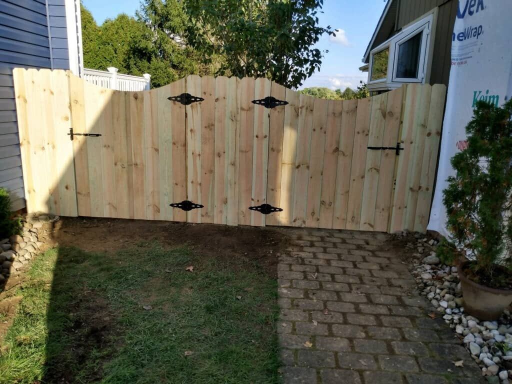 Wooden gate across a backyard path, with grass on one side and brick pavers on the other.