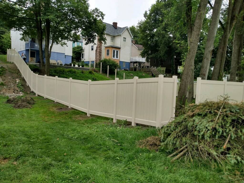 Beige fence along a grassy yard with trees and houses in the background