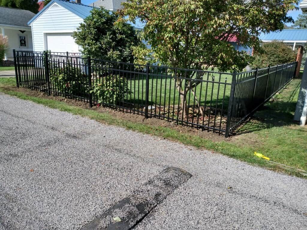 Black metal fence around a grassy yard beside a house, along a gravel street.