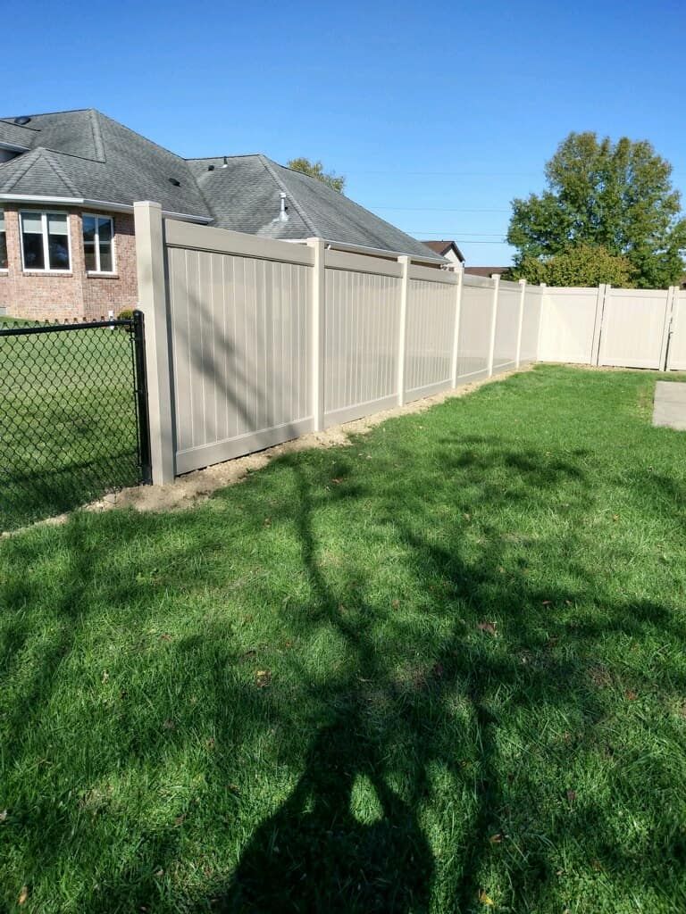 Backyard with green grass and a tan privacy fence beside a brick house under a clear blue sky