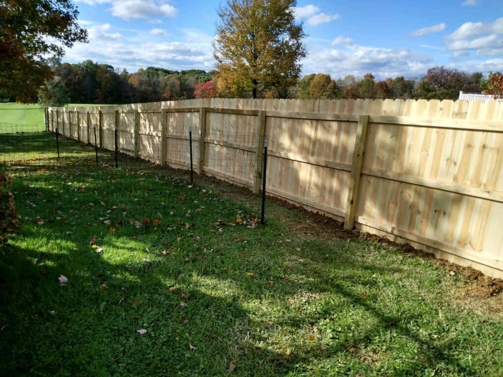Wooden privacy fence along a grassy yard with trees and blue sky in the background