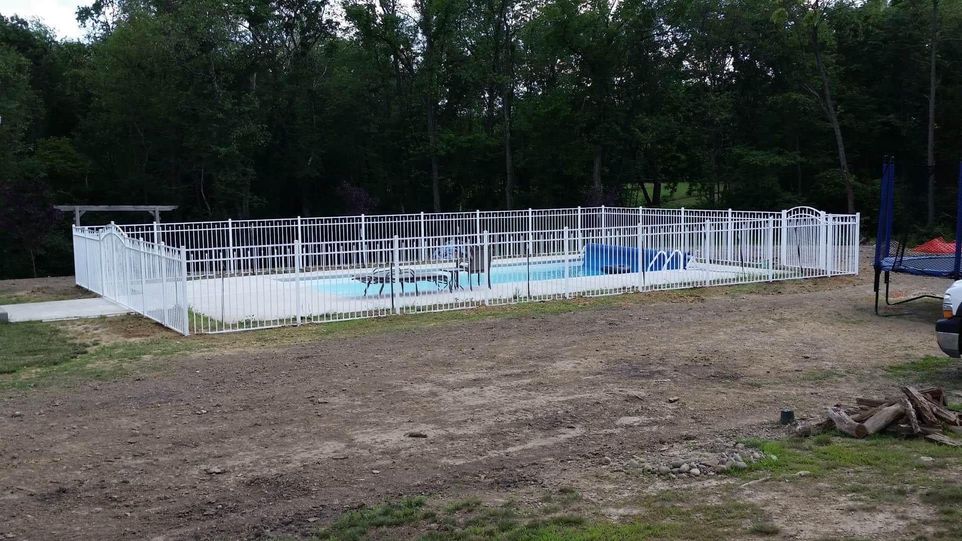 Small above-ground pool with white fence and blue water in a wooded backyard.