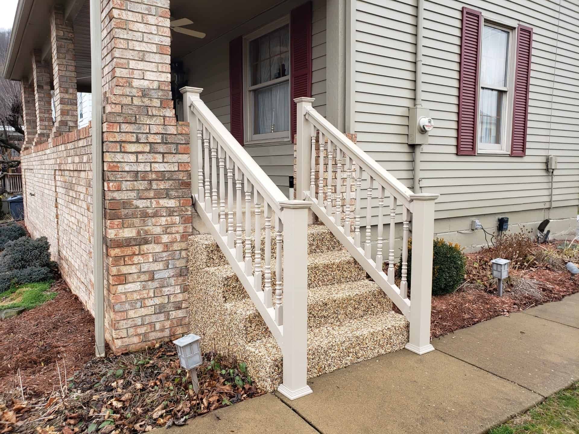 Front porch stairs with white railings on a brick and beige house, beside a sidewalk.