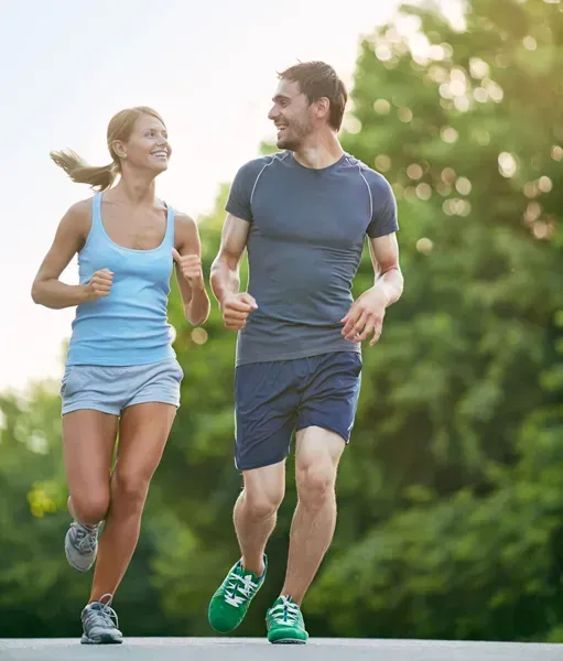 Two runners in blue athletic wear jogging together on a tree-lined path outdoors