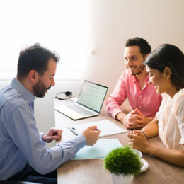 Three people in a bright office meeting around a table with a laptop and documents.