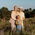 Three people standing in a sunny wildflower field, two adults behind a child in overalls.