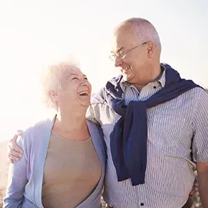 Smiling couple outdoors, arm in arm in bright sunlight, looking at each other