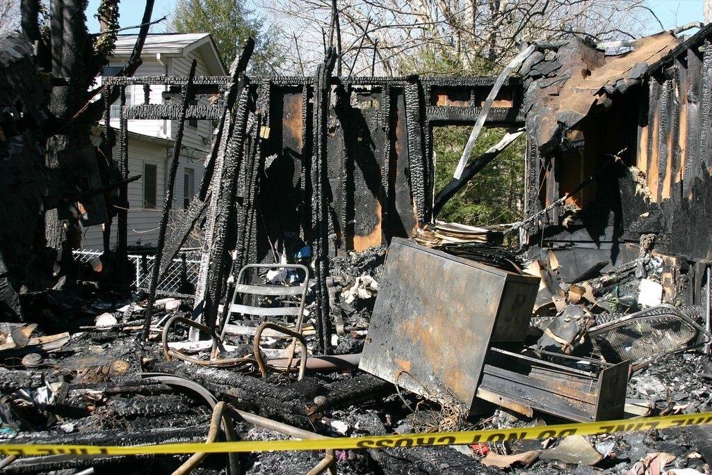 Vestiges calcinés d'une structure après un incendie, avec des poutres noircies et des débris