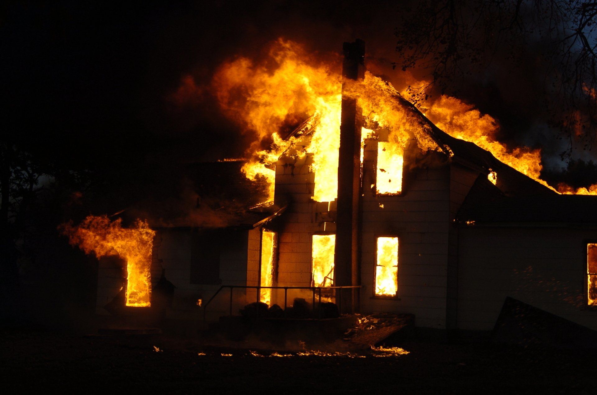 Une maison blanche à deux étages, engloutie la nuit par d'intenses flammes orange vif.