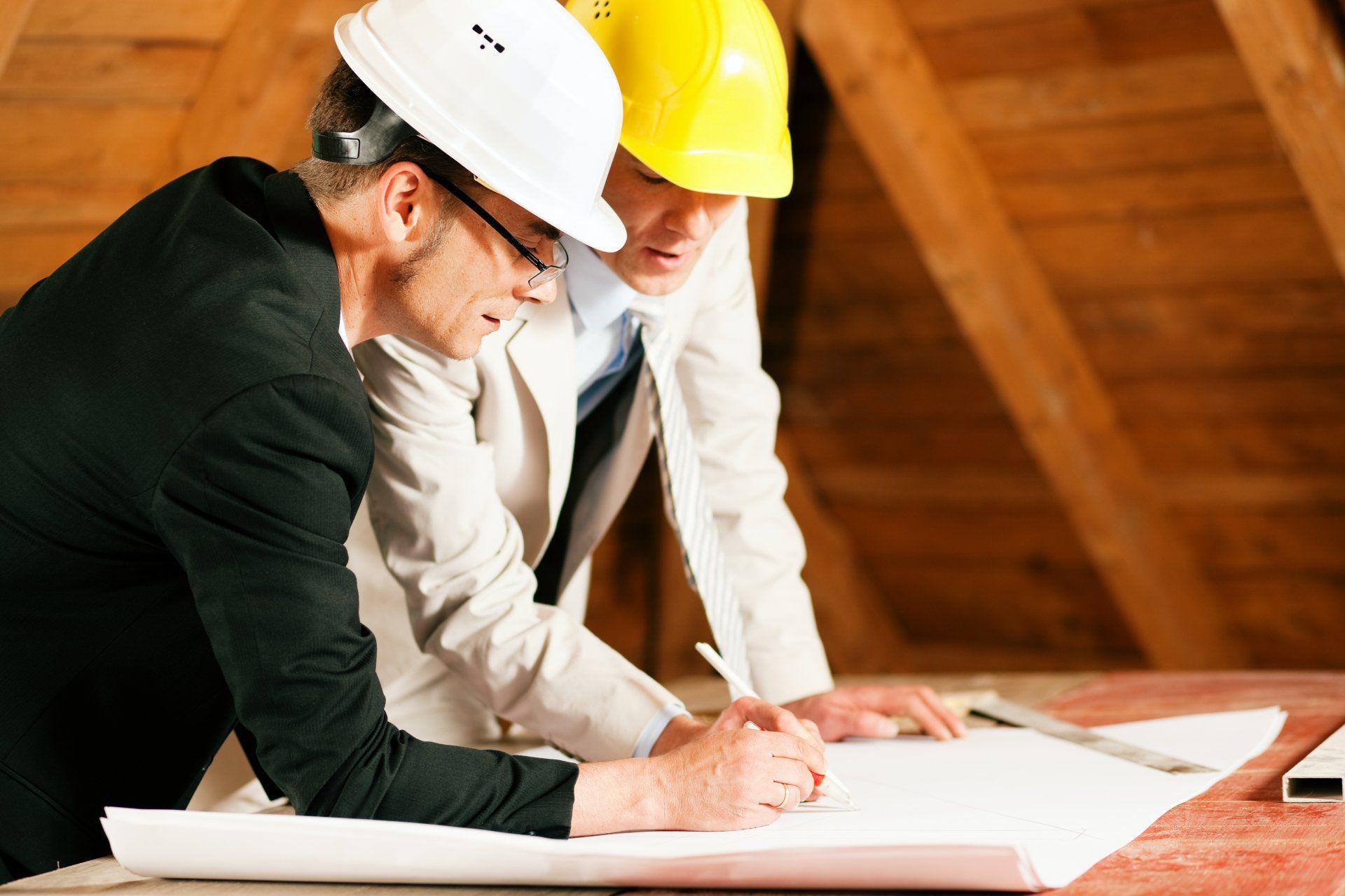 Deux personnes portant des casques de chantier examinent des plans dans un grenier.