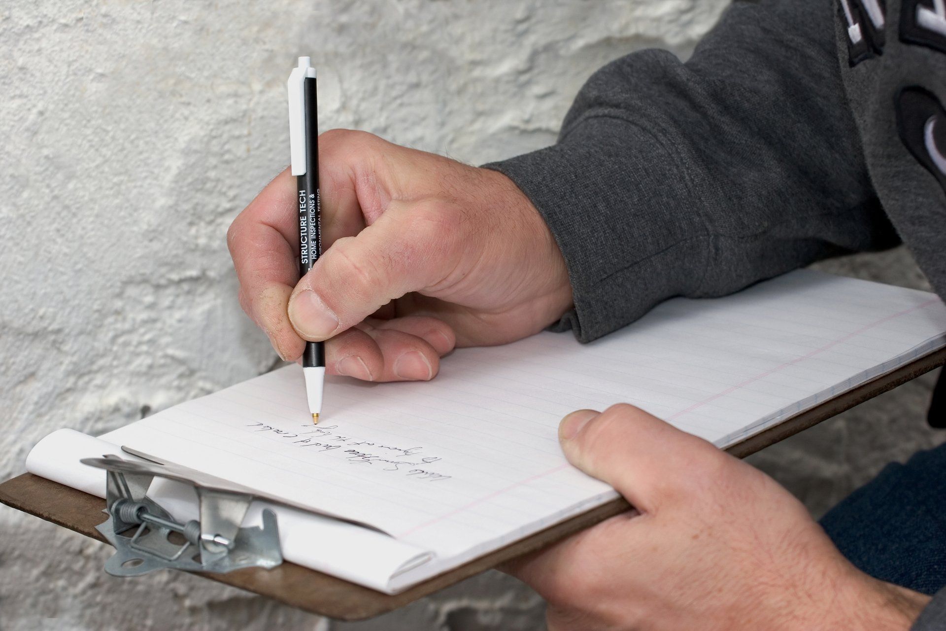 Person writing on a clipboard, possibly taking notes on a white stone wall.